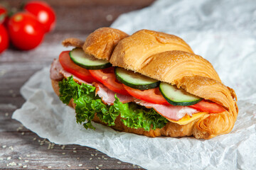 Breakfast of Fresh croissant with ham, cheese and salad leaf on white wooden background.