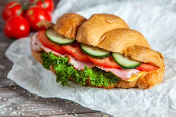 Breakfast of Fresh croissant with ham, cheese and salad leaf on white wooden background.