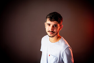 Obraz premium Young boy standing and looking at camera, in plain gray shirt and reddish lighting background.
