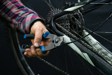 Obraz premium Mountain bike repair in the workshop. Mechanic's hands and tool close-up. The mechanic cuts off the old rear derailleur cable. A small business in the garage.