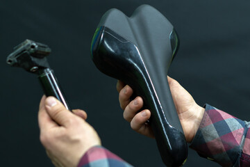 A mechanic in a bicycle workshop repairs mountain and road bikes. The mechanic is holding a new saddle and seatpost on a black background. New components for the bike.