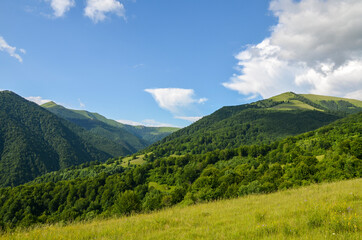 Beautiful landscape of green mountains, grassy field and rolling hills with cloudy blue sky. Carpathians, Ukraine