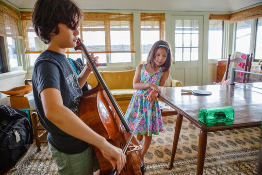 A boy gives cello concert to small mouse in box while sister watches