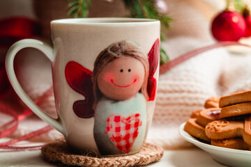 A cup of hot tea with the image of a cute angel on the windowsill against the background of fir...