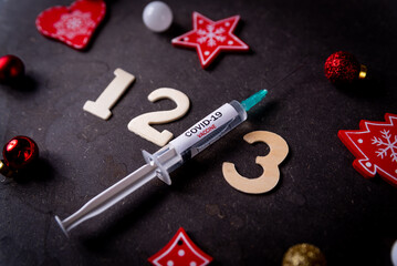 Third covid vaccine dose and jab concept and numbers and Christmas decorations. Syringe is seen on...