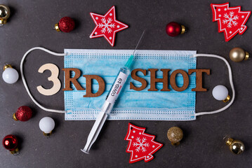 Third covid vaccine dose and jab concept with face mask and Christmas decorations. Syringe is seen on table as a concept for the 3rd covid-19 vaccine dose, also called booster shot
