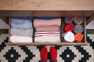 Woman near open drawer with folded clothes indoors, top view. Vertical storage