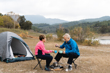 Senior couple eating and camping after trekking day at the lake - Focus on woman face