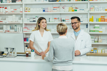 Twee apothekers die voorgeschreven medicijnen geven aan senior vrouwelijke klant in een apotheek