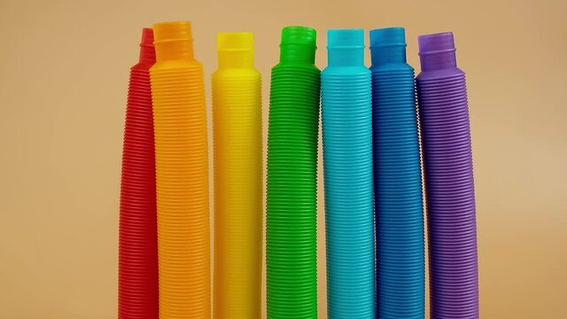 Group of multicolored rainbow toy pop it tube falls and rolls on beige background, trend toy for the development of fine motor skills of hands, anti stress crackling tube.