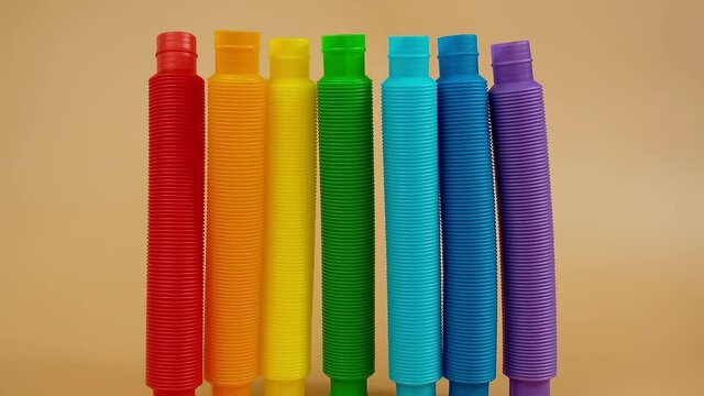 Group of multicolored rainbow toy pop it tube falls and rolls on beige background, trend toy for the development of fine motor skills of hands, anti stress crackling tube.