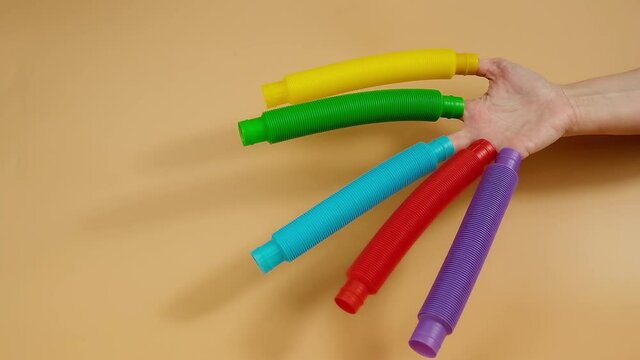 Group of multicolored rainbow toy pop it tube in hand on beige background, trend toy for the development of fine motor skills of hands, anti stress crackling tube.