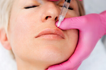 Lips augmentation procedure. Close-up portrait of beautiful adult woman getting injection at beaty...