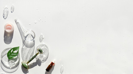 Beauty treatment banner. Jade stone face roller with monstera leaf, orchid flowers and glass baubles. Pink moisturizer cream in jar. Sunshine, long shadows. Beauty treatment flat lay with copy-space.