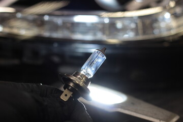 Halogen light bulb H4 above the black car. A professional worker changes the new halogen lamps of...