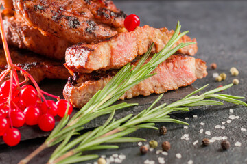Hot steak with rosemary, salt, pepper, red berries on a stone board. Close-up juicy meat, grilled, barbecue.