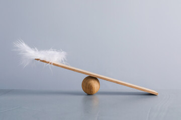 Wooden ball, small plank and feather on grey background. Balance concept