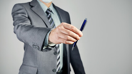 Hand of businessman in suit holds pen close-up and shows, on copy space on gray background