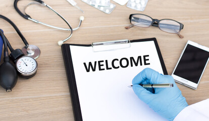 text on a white welcome sheet on the table, the inscription is written by the doctor's hand next to the phone, stethoscope glasses