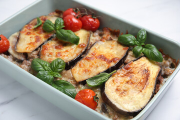 Delicious eggplant lasagna in baking dish on white marble table, closeup