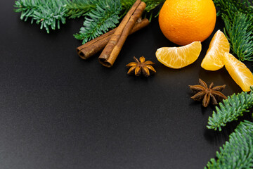 New Year's background. A branch of fir, tangerines and spices for mulled wine on a black background.