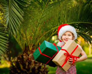 a small, beautiful girl in Santa's clothes, standing with gifts in her hands,near green palm trees, at New Year's time, in a southern country