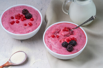 Whipped semolina mousse with berries in a white glass on a white table.
