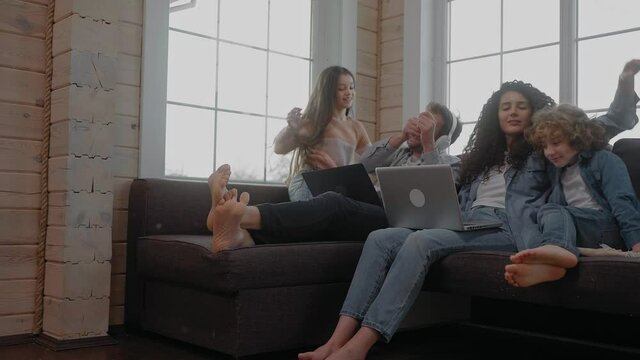 Children to their parents working sitting on a couch to hug and sit together. Young family spends time together. Working from home with children in lockdown. 50 fps. High quality 4k footage