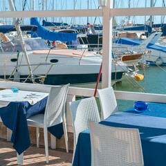 A fragment of a coastal cafe on the Black Sea embankment against the backdrop of moored modern boats and yachts. Sochi. Russia