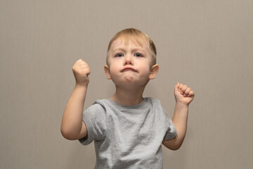 Cute boy in gray t-shirt blond European German age 3 years isolated on gray background shows and communicates for advertisement layout, close-up layout with selective focus and blurred background