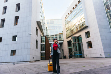 Latin business woman talking on the mobile phone and carrying a suitcase in the street.