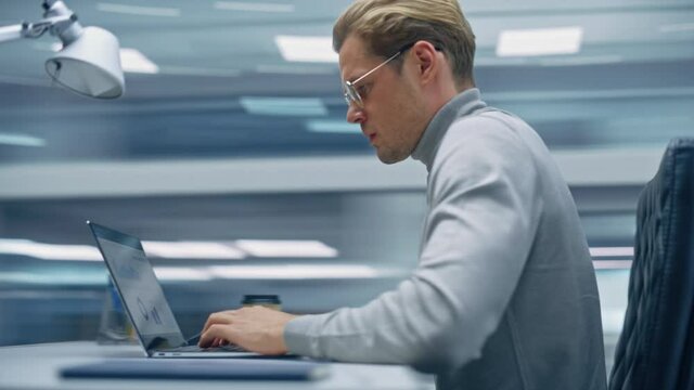 Modern Office: Handsome Businessman Sitting at His Desk Working on a Laptop Computer. Man working with Big Data e-Commerce Analysis. Energetic 360 Degree Fast Tracking Shot. Camera Moving Around