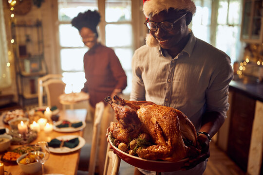 Happy African American man serves roast turkey for Christmas dinner at home.