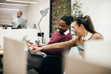 Multi-ethnic business coworkers have fun while using laptop on break in office.