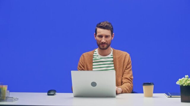 Blue Screen Office Background: Caucasian Businessman Sitting at His Desk Working on a Laptop Computer. White Man working with Big Data e-Commerce Analysis. 360 Degree Tracking Shot. Moving Around