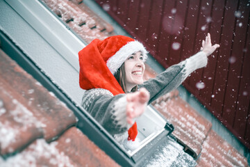 Young woman in a red and white Christmas hat looking out of a skylight window and smiling, totally...