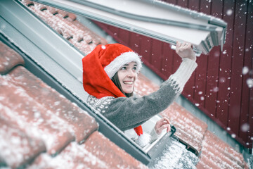 Young woman in a red and white Christmas hat opening a skylight window and smiling, excited about...