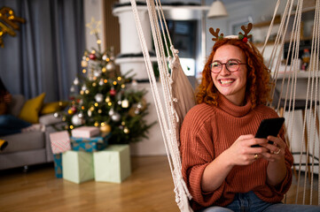 Smiling young woman using his phone by Christmas tree