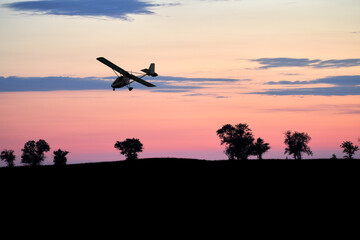 Fototapeta na wymiar Prairie with acacia trees at sunset. A sports plane is flying across the sky. Night shooting. Selective focus. Copy space.
