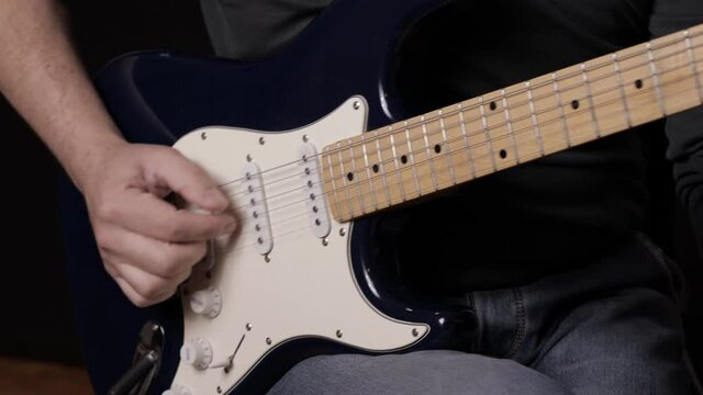 A male musician plays a melody on a blue six-string guitar.