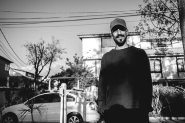 Handsome, young and happy caucasian guy with trucker hat standing and smiling in a park in the afternoon (in black and white)