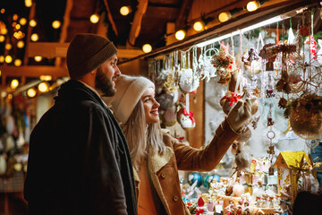 Christmas, winter holidays, vacation, travel, purchase conception: happy smiling couple shopping at festive street market, choosing gifts.  Outdoor night portrait. Copy, empty space for text
 - obrazy, fototapety, plakaty