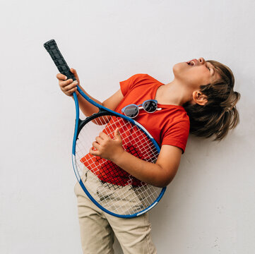 Blond boy in t-shirt plays his racket as if it were a guitar