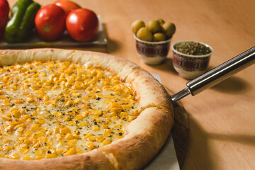 Close-up of a corn pizza with stuffed rim on a light wood table.