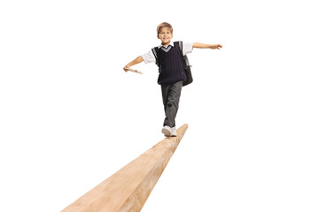 Schoolboy in a uniform holding a book and walking on a wooden beam