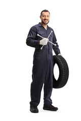 Full length portrait of an auto mechanic holding a tire and a lug wrench