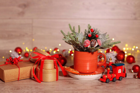 festive decor on a wooden table orange cup with dried fruits. wrapped gifts with a red ribbon. tree branches garland red decorative paravoz. christmas concept