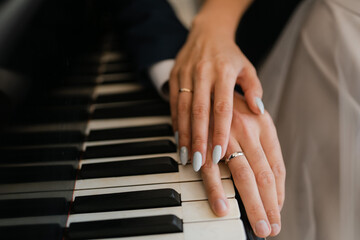 the hands of the newlyweds on the piano keys,
wedding engagement rings on fingers, close-up of...