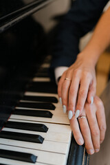 Fototapeta na wymiar the hands of the newlyweds on the piano keys, wedding engagement rings on fingers, close-up of couple's hands with rings