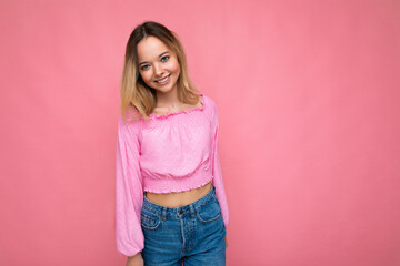 Portrait of young beautiful smiling hipster blonde woman in trendy pink crop top blouse. Sexy carefree female person posing isolated near pink wall in studio. Positive model with natural makeup. Copy